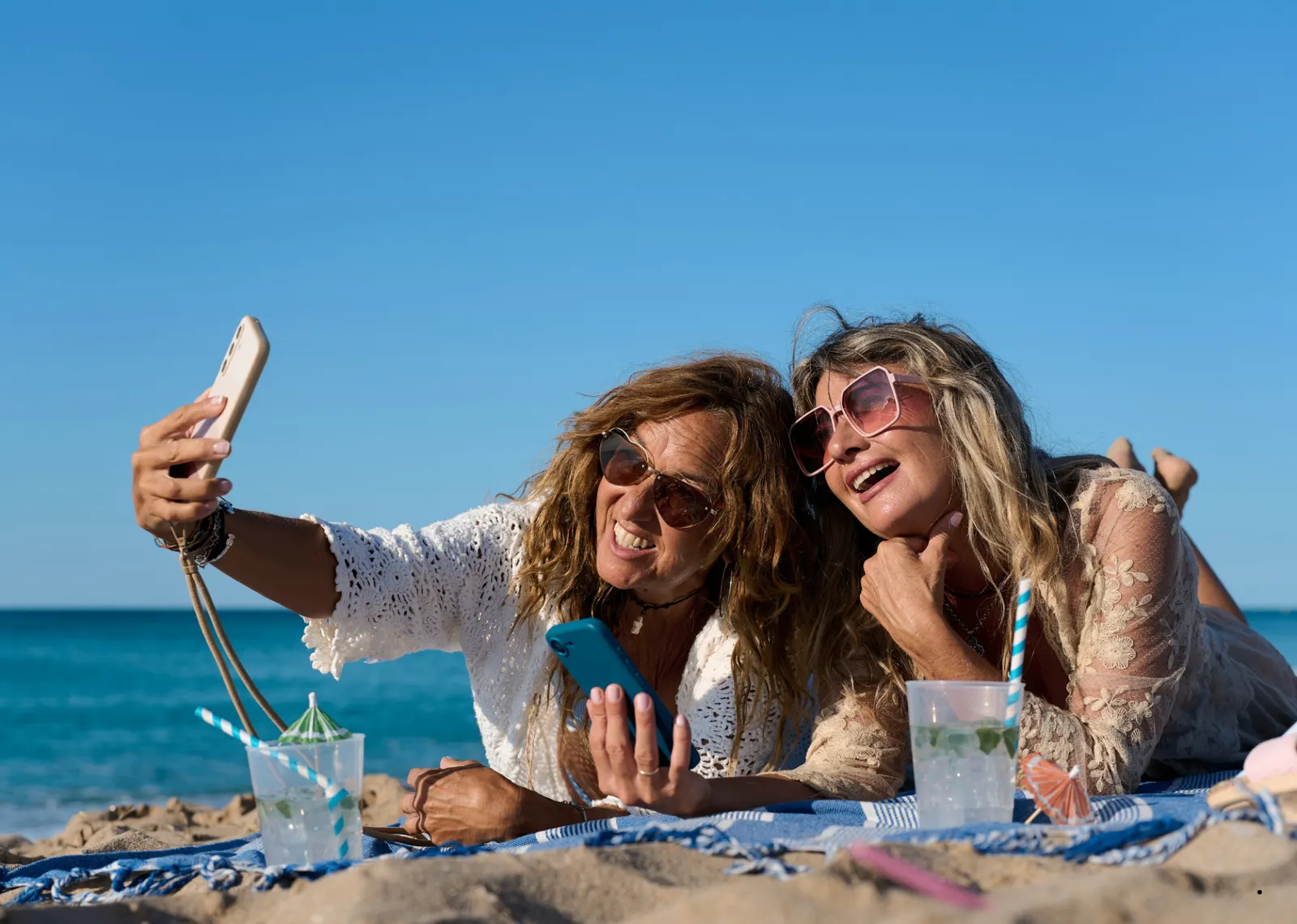 Two friends taking a selfie on a Tunisian beach with their phones