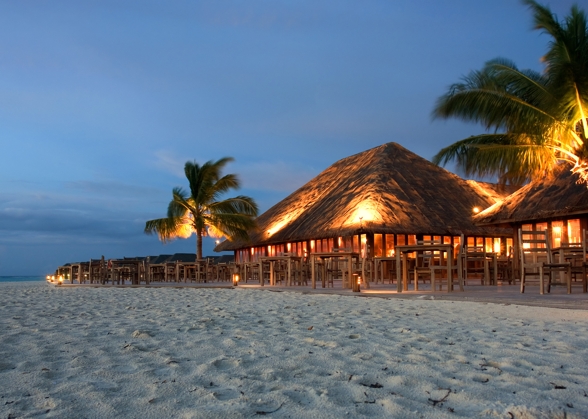 Palm-thatched umbrella and seaside tables at sunset